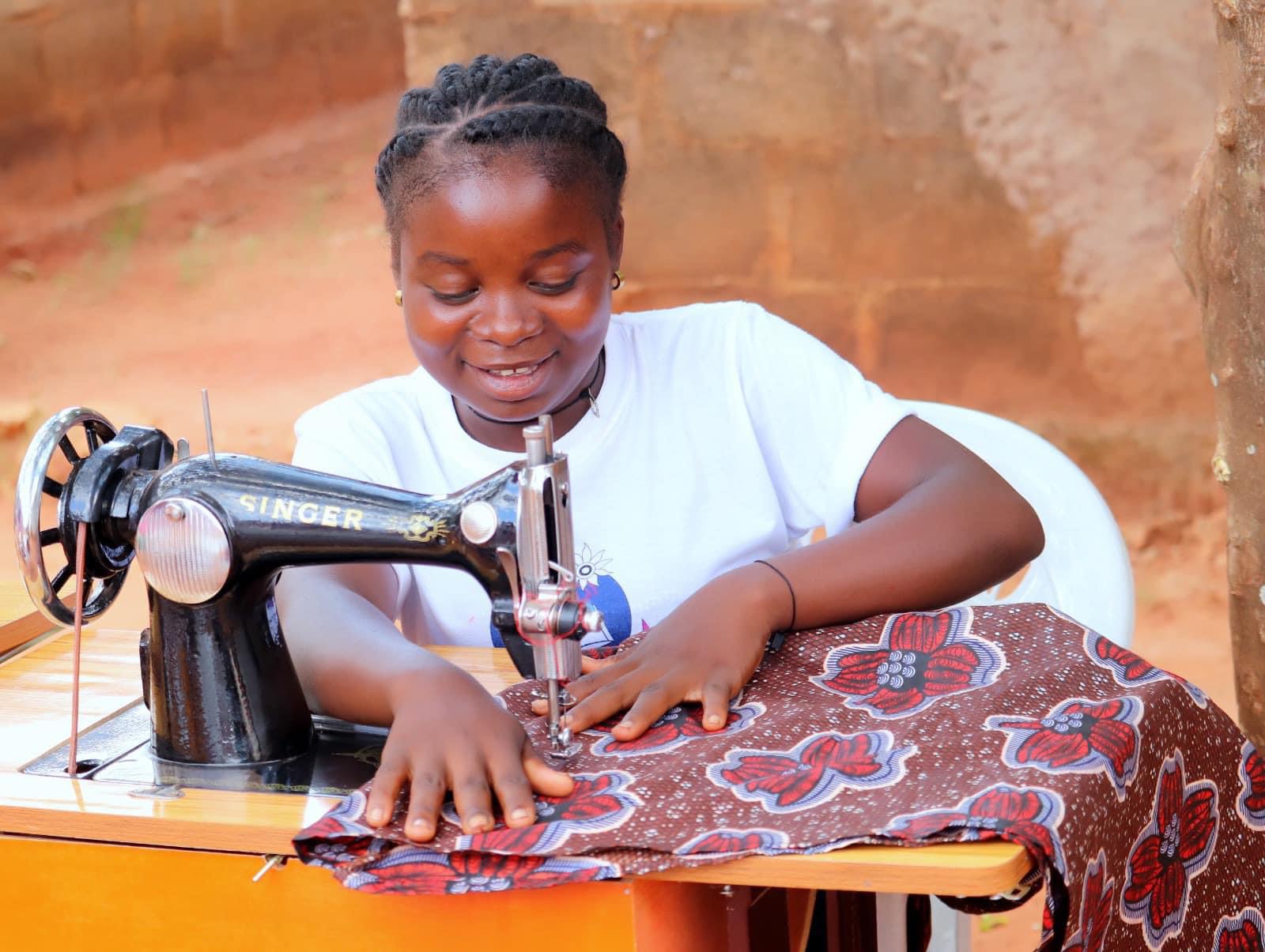 A young girl smiles as she uses a sewing machine.