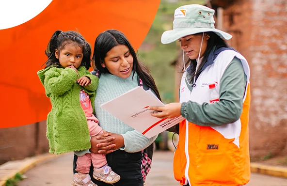A World Vision staff member reviews documents with a mother holding a child in a rural village.