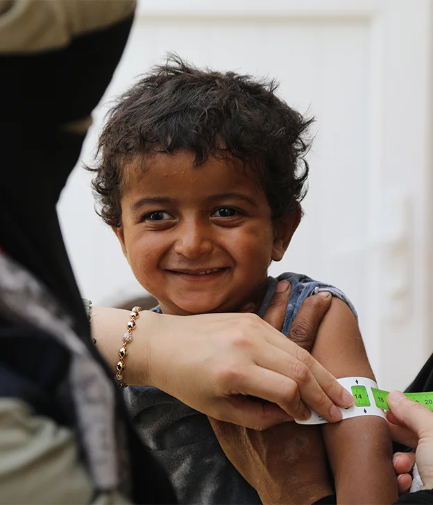 A health worker measures a young child’s upper arm with a medical measuring tape.
