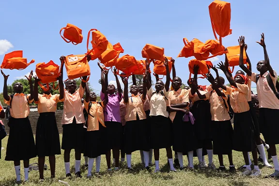 Adolescent students stand outdoors holding bright orange hygiene kits distributed by World Vision.