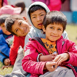 A group of children sit in a line on the grass during an outdoor group activity.