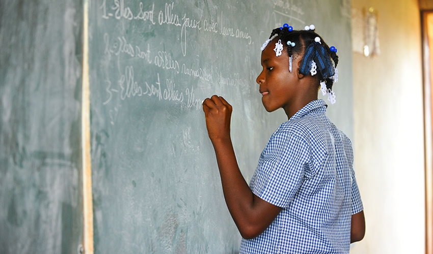 A Haitian girl stands and writes on a chalkboard in her classroom. She was a child labourer but is in school again.