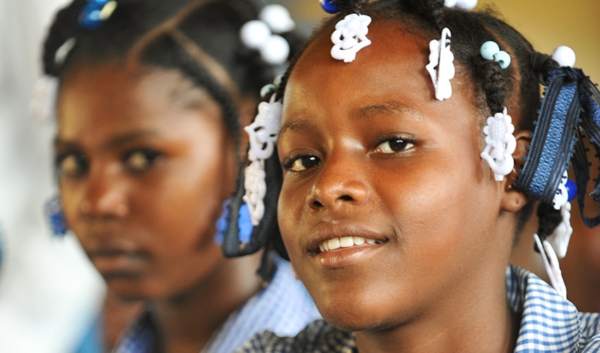 A girl sits in a classroom with a classmate behind her, in Haiti.