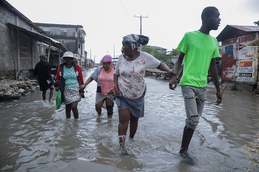 Four adults wade through a flooded street. They escape to higher ground after Hurricane Melissa struck in Haiti.
