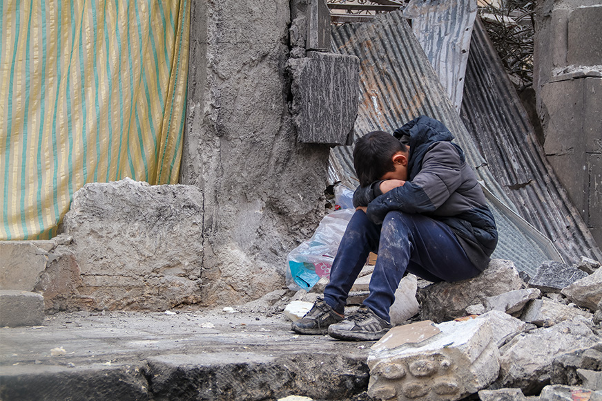 A boy sits with his head in his hands, surrounded by city ruins in Aleppo, Syria.