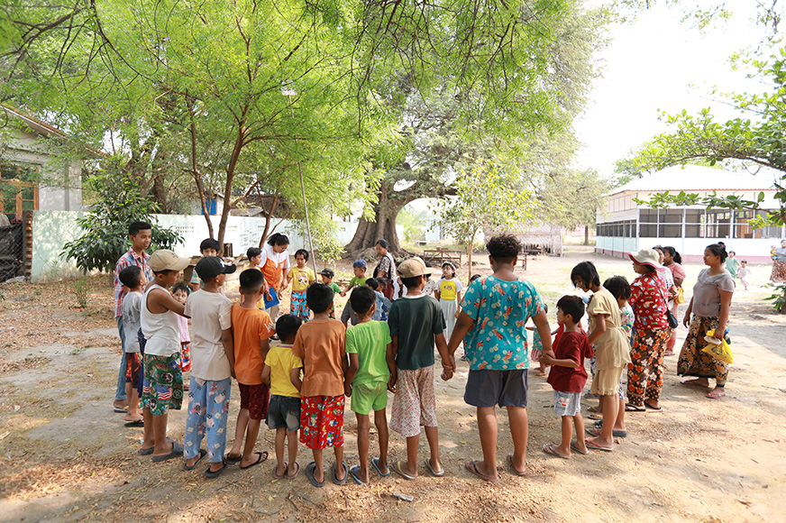 A group of children stand together and hold hands outdoors in Myanmar.