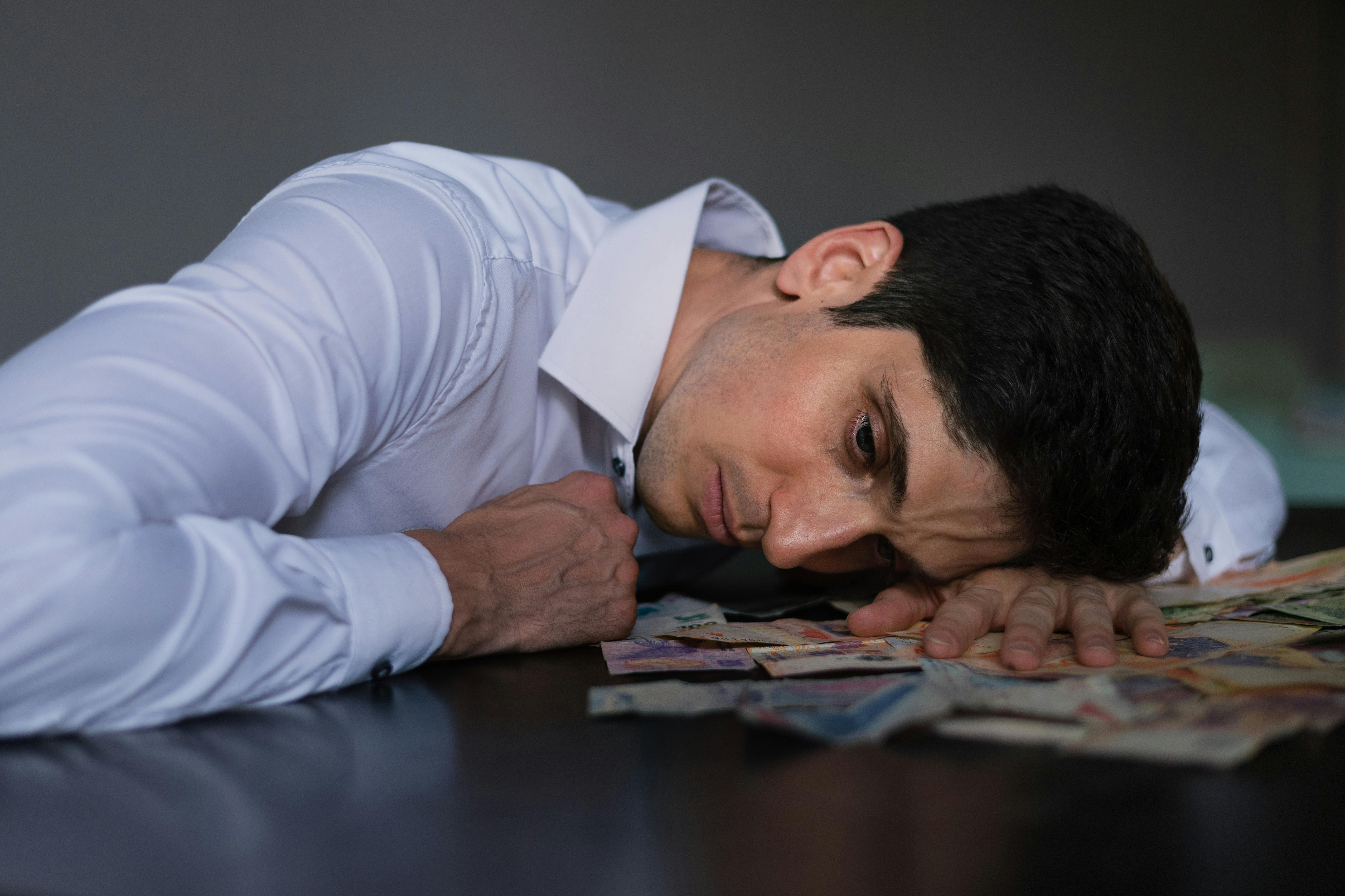 A person in a white button-down shirt lies with their head resting on a dark table.