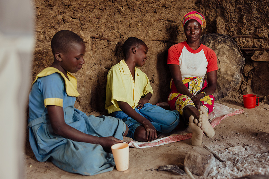 Hungry, a worried mother sits in her small hut with her son and daughter in school uniforms.