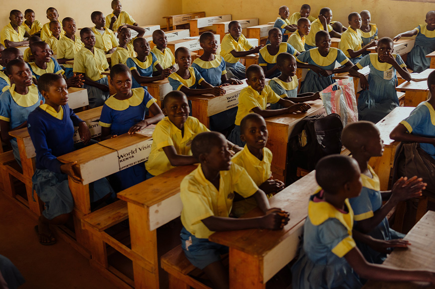 A large group of students sit at desks in a school classroom.