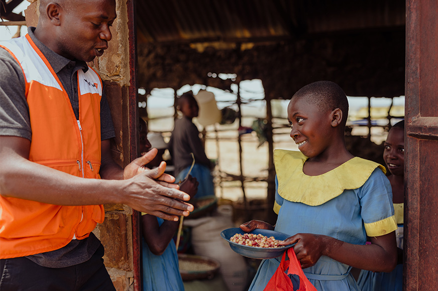 A girl in a school uniform holds a nourishing meal and speaks with a World Vision worker.