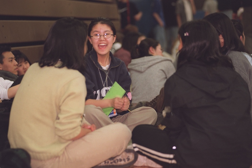A group of teens sit cross-legged on the floor.
