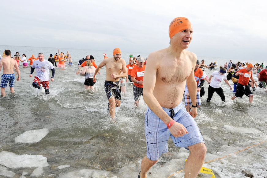 A large group of people run into and out of a cold lake, wearing orange World Vision swim caps.