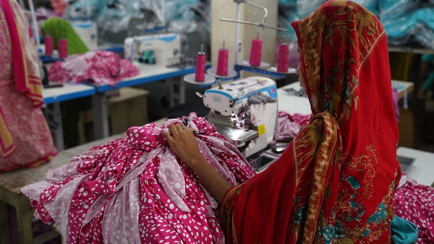 A factory worker sits behind a table piled with pink fabric.