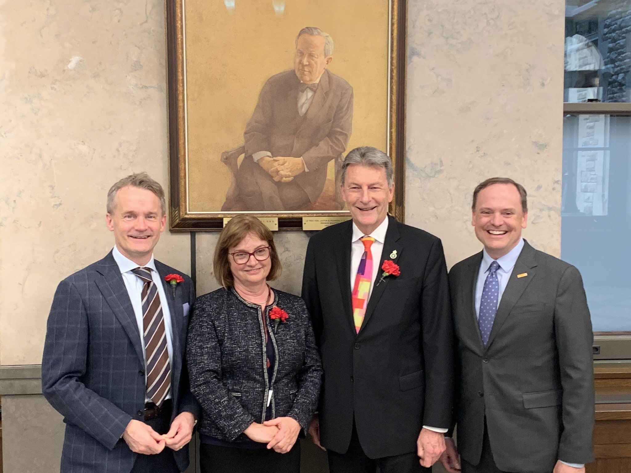 Four adults wearing suits pose for a photo.