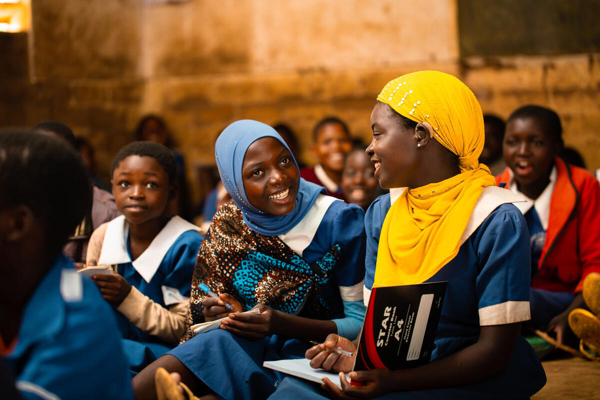 Students in blue school uniforms sit together, including a student wearing a yellow headscarf with a visible hearing aid. (Malawi, 2025)