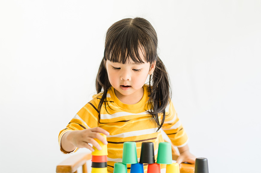 A toddler stacks multi-coloured cups.