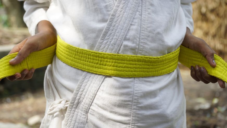 Closeup of a child’s waist, as they tighten their yellow karate belt with their hands.