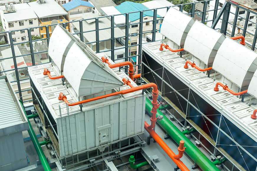 Rooftop industrial cooling units with orange and green piping, used for temperature control in a densely populated city area.