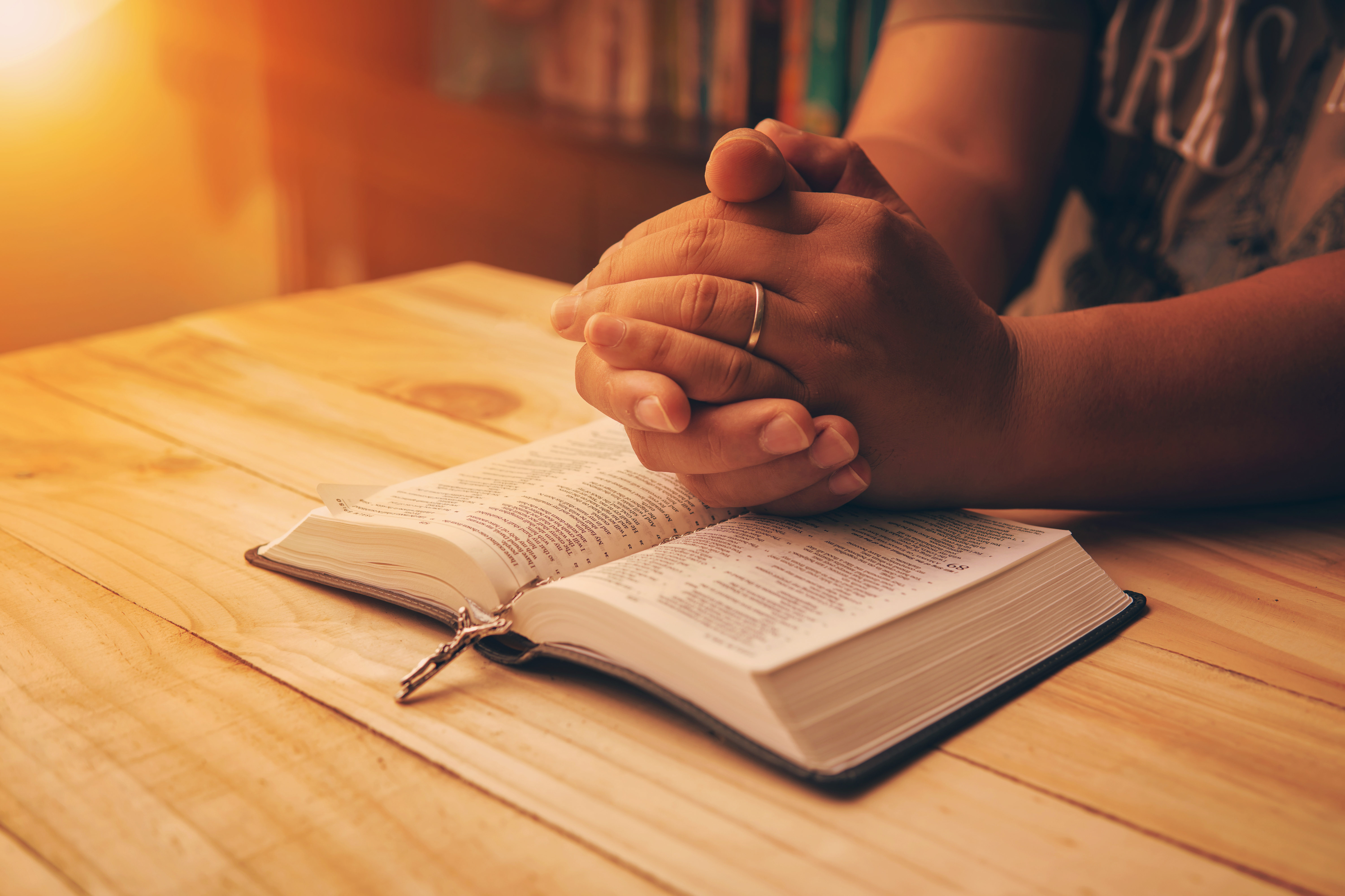 A person sits with folded hands on top of their Bible, symbolizing prayer and devotion.