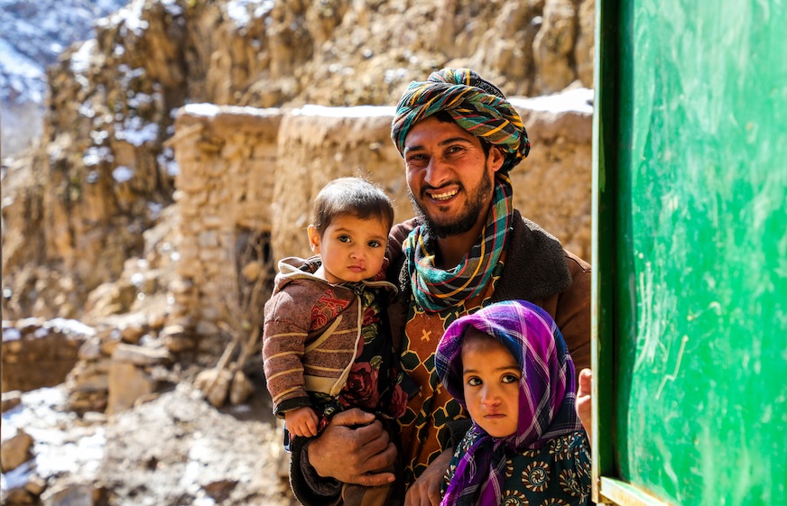 A father wearing a turban smiles with his two young children.