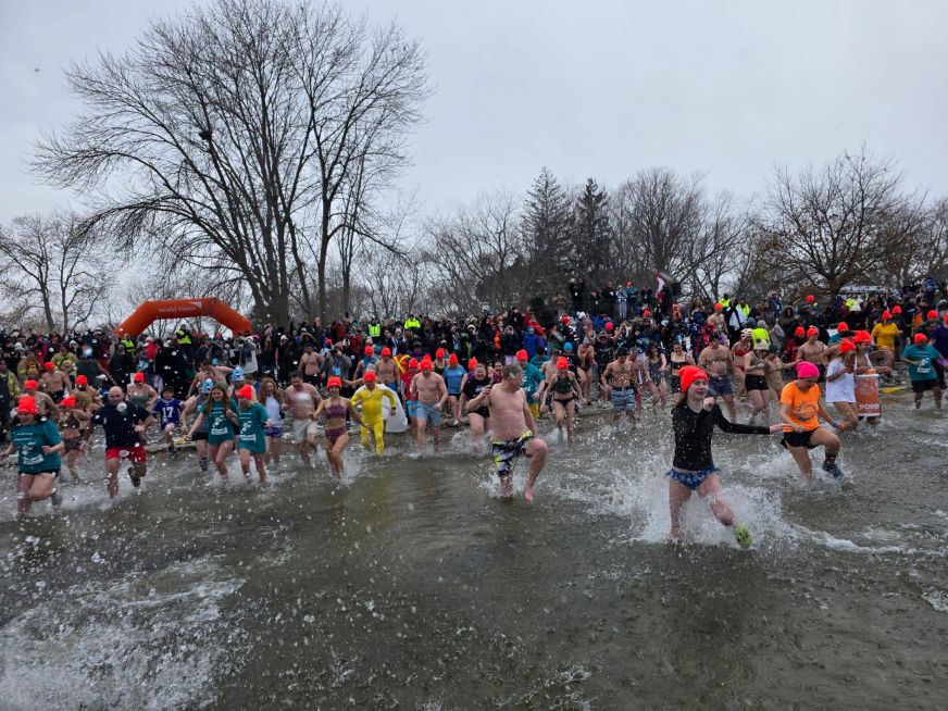 A large group of people wearing bright orange hats run into Lake Ontario.
