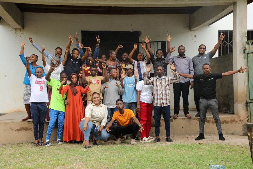 In Tanzania, a group of AHADI participants pose for a photo with their hands up.