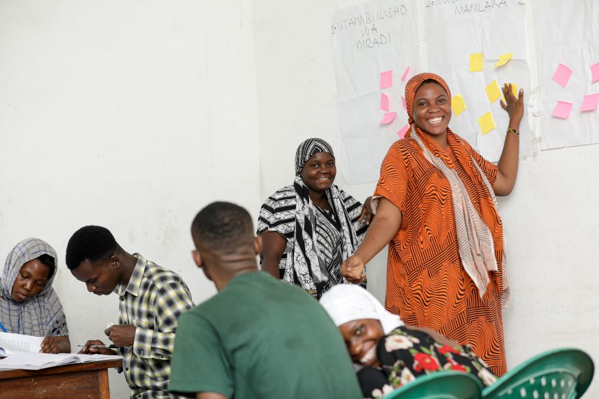 In Tanzania, a female participant in the AHADI project puts sticky notes on the wall during a collaborative session.
