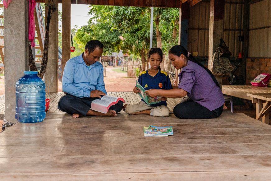 A Cambodian family of three sits on the floor, reading together.