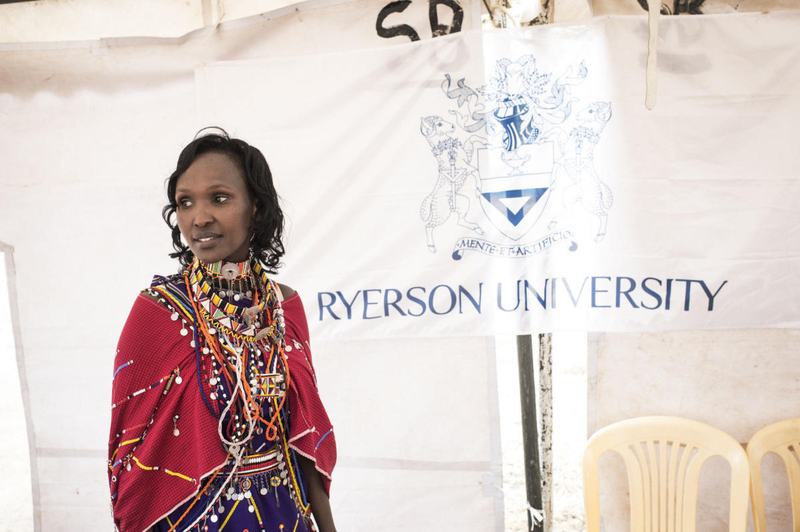 A young woman in bright dress smiles off-camera in front of a Ryerson University banner.