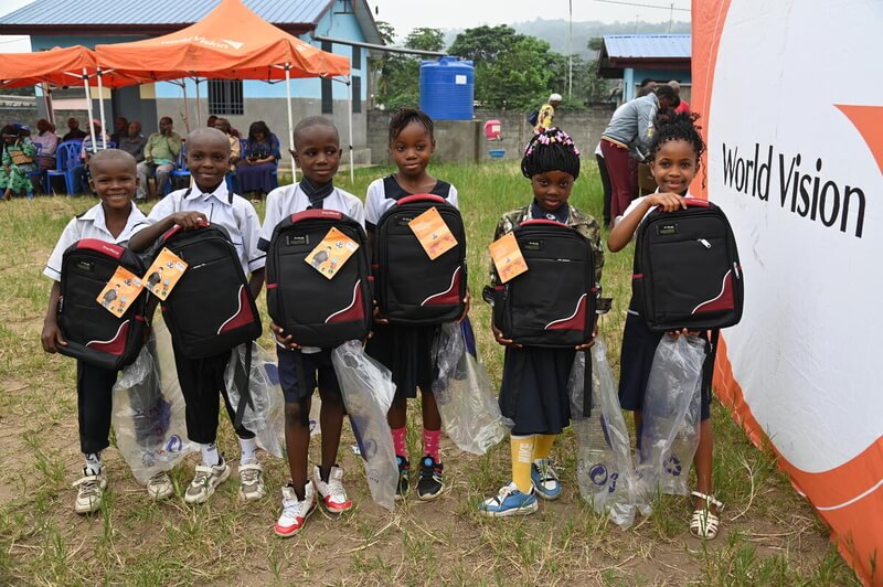 Six children holding school bags surrounded by World Vision banner