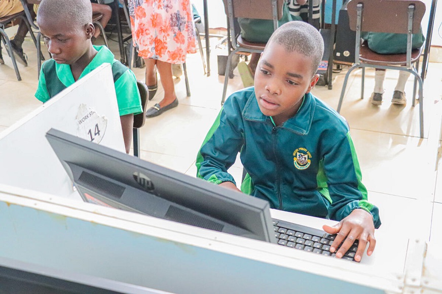 A young student wearing a green uniform uses a desktop computer. (Zimbabwe, 2025)