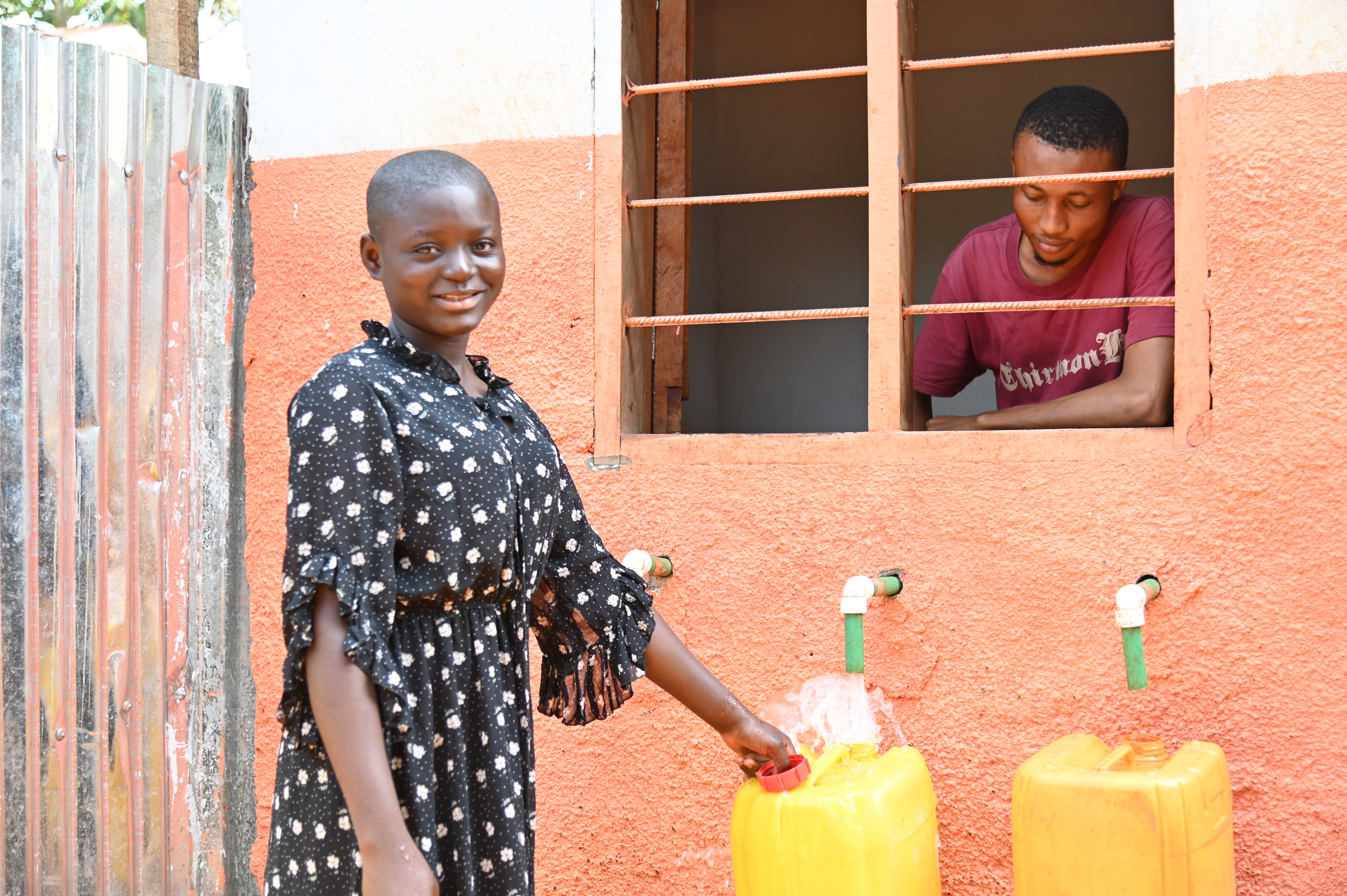 A young girl stands beside a tap, filling a yellow bucket with water.