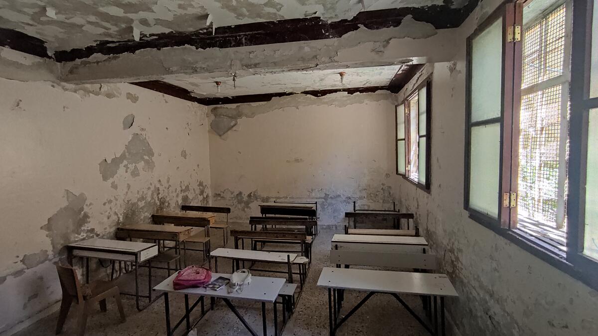 Rows of empty desks sit in an old, dilapidated classroom (Syria, 2022)