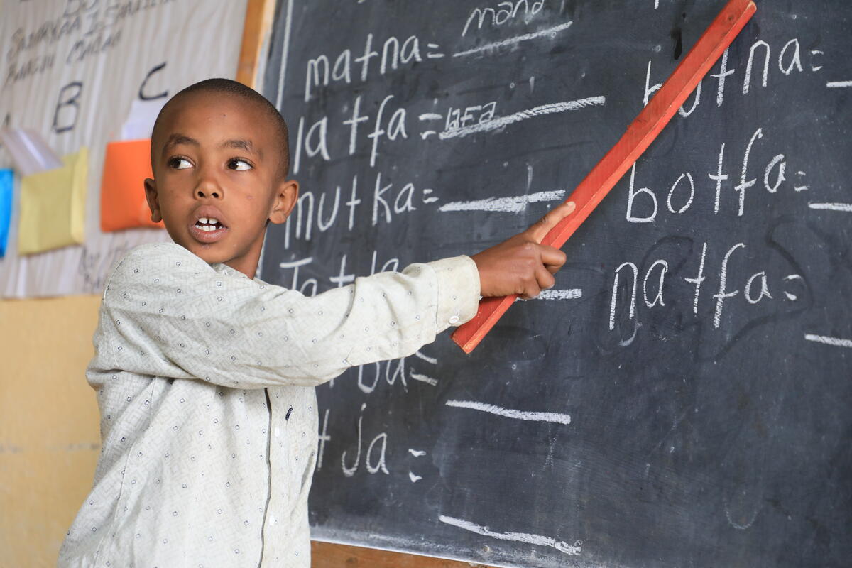 A young child holding a pointer stick in front of a blackboard (Ethiopia, 2025)