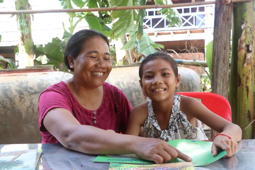 In Cambodia, a woman and young girl sit in front of a book, smiling.