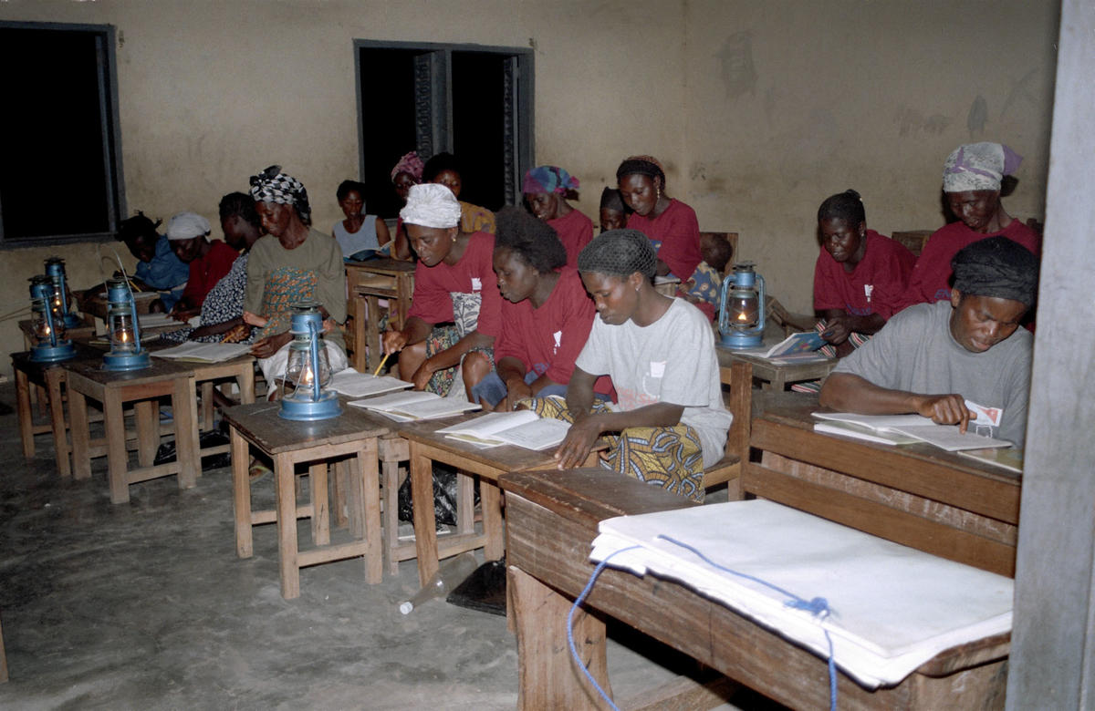 Group of women seated at wooden desks studying in a classroom setting with lamplight.