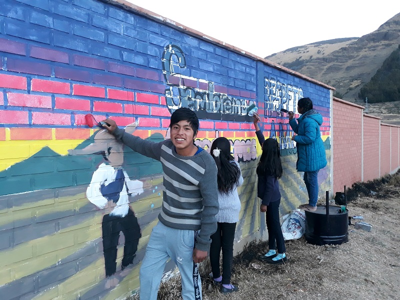 Four young people in Bolivia paint a mural on a building.