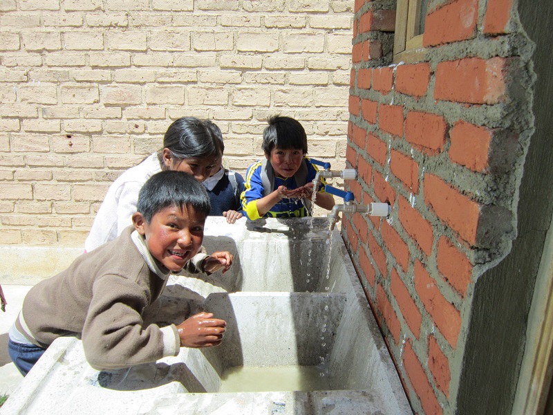 Three children in Bolivia wash their hands at an outdoor tap.
