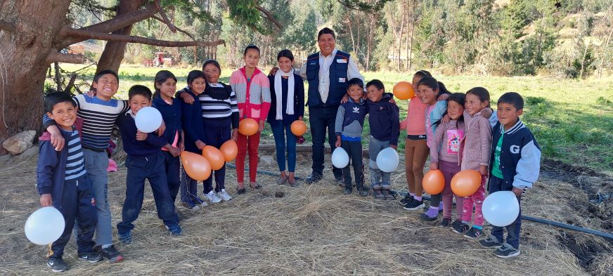 A group of children holding balloons stand with a man in a World Vision vest.