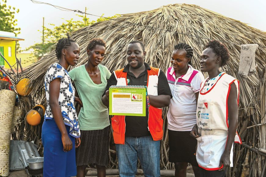 A group of women gather around a man in a World Vision vest to read a flip book.