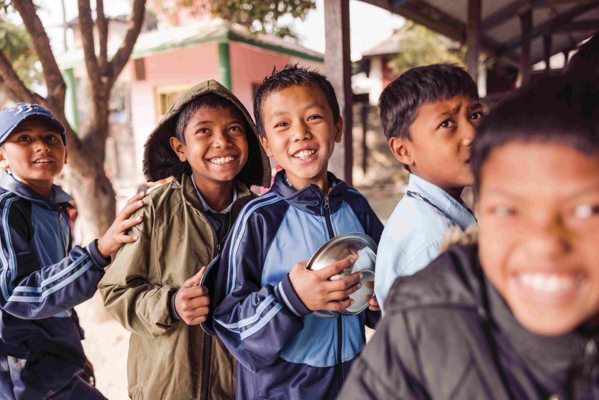 A group of boys wait in line, smiling, in Nepal.