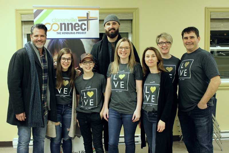A group of Canadian teen and adult volunteers stand close together while smiling for the camera. Most are wearing grey T-shirts with “love” printed on the front