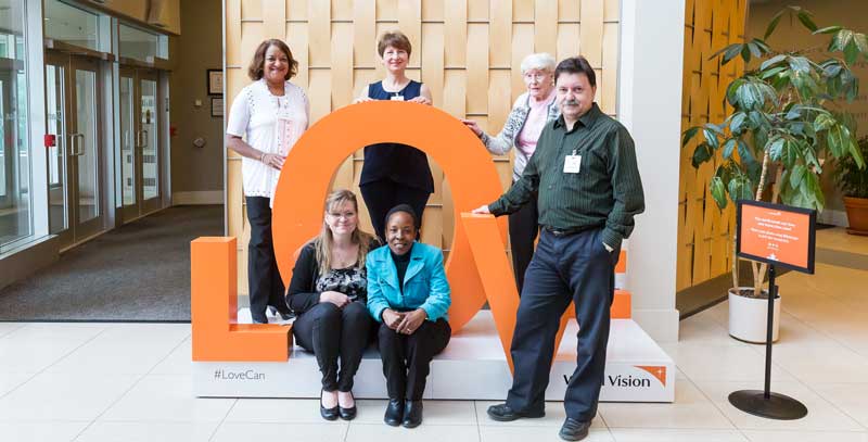 A man and five women pose with a display that reads "Love" in the World Vision Canada lobby.