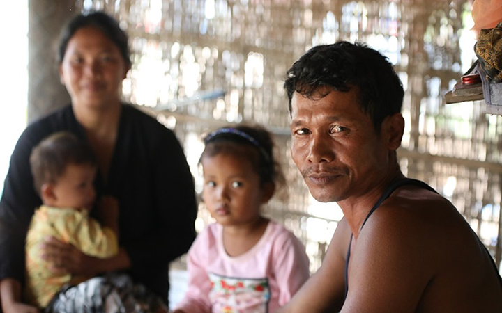 A man faces toward the camera. Behind him are a woman and two young children.