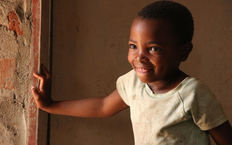 A young Zambian girl smiles in a doorway.