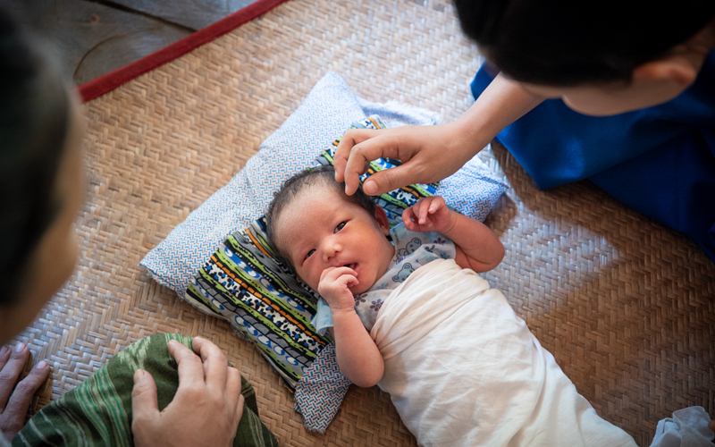Two women from Myanmar look down at a tiny baby.