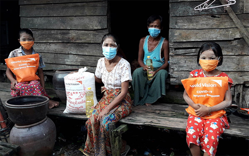 Thandar from Myanmar sits in front of her house with her family and their supply of nutritious ingredients from World Vision.