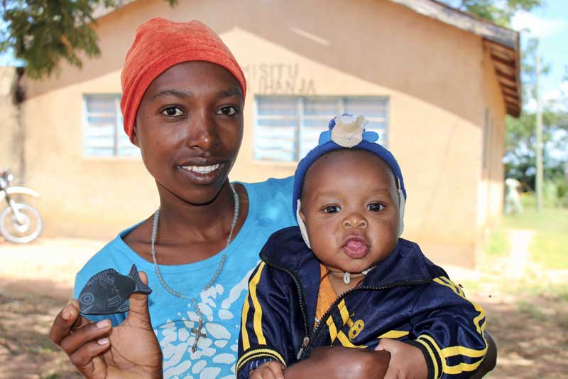 A woman in Tanzania holding her baby and showing off an iron fish.