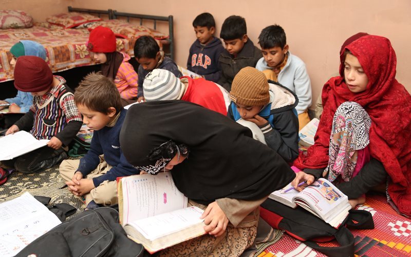 a group of children sit on the floor all looking down at school books.