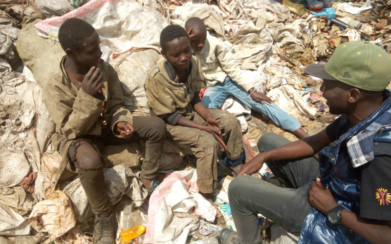 A group of four young men sit on a pile of garbage.